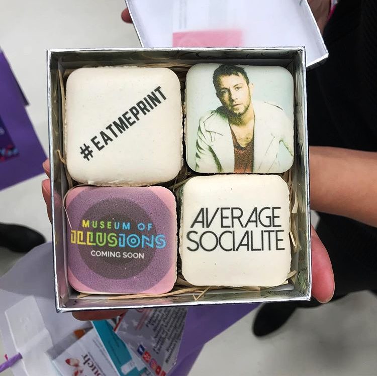 An open box of four square macarons printed with Museum of Illusions and Average Socialite artwork